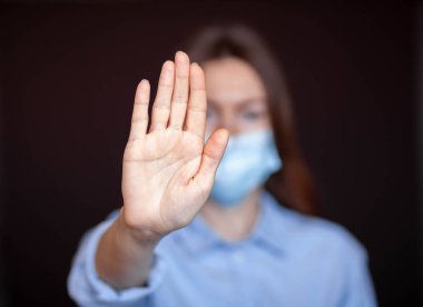 Coronavirus konsepti. Hastalıktan korunmak için maske takan ve Corona virüsünü durdurmak için el hareketi yapan bir kız. Evde kalmak için küresel çağrı. Aşıyla salgını durdurun.