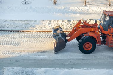 Büyük turuncu traktör yoldan kar temizler ve kamyona yükler. Kışın kardan şehrin yollarının temizlenmesi ve temizlenmesi