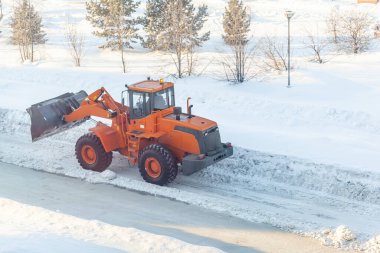 Büyük turuncu traktör yoldan kar temizler ve kamyona yükler. Kışın kardan şehrin yollarının temizlenmesi ve temizlenmesi