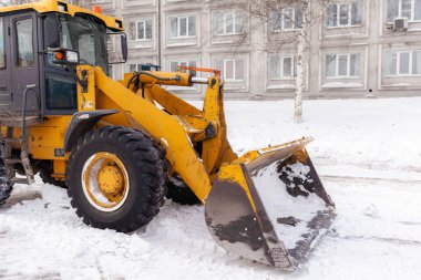 Büyük turuncu traktör yoldan kar temizler ve kamyona yükler. Kışın kardan kentteki yolların temizlenmesi ve temizlenmesi. Kar yağışı ve kar fırtınasından sonra karlar kalkar. 