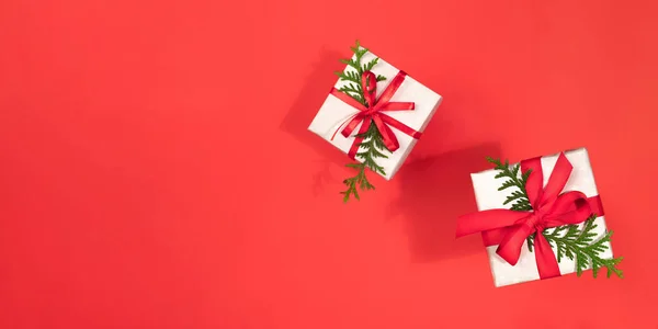 Caixas de presente decoradas com fitas e galhos verdes de arborvitae no vermelho. Banner de Natal. Espaço de cópia. — Fotografia de Stock