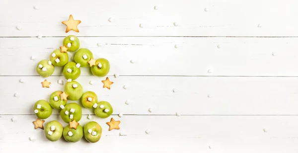 Árbol comestible de Navidad de manzanas verdes con galletas en forma de estrella y malvaviscos sobre mesa de madera blanca. — Foto de Stock