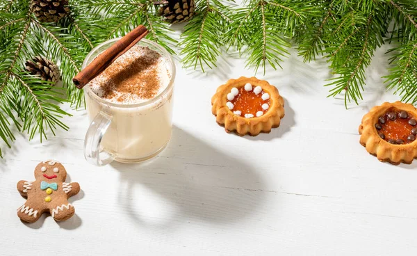 Tatil tatlılarıyla Noel imajı. Geleneksel ev yapımı tarçınlı yumurta likörü, zencefilli adam, beyaz ahşap zemin üzerinde yeşil köknar dallı zencefilli kurabiye, koni. Uzayı kopyala Yatay çekim.