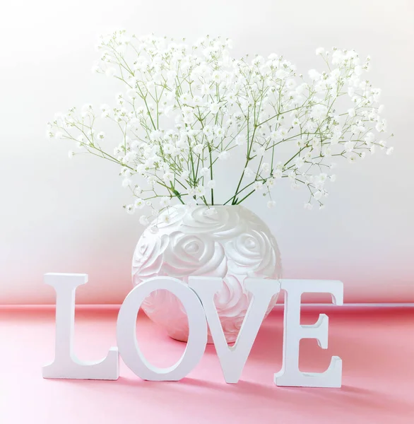Lettere bianche AMORE con arte vaso rotondo di fiori di gypsophila bianchi su rosa-bianco. Da vicino.. — Foto Stock