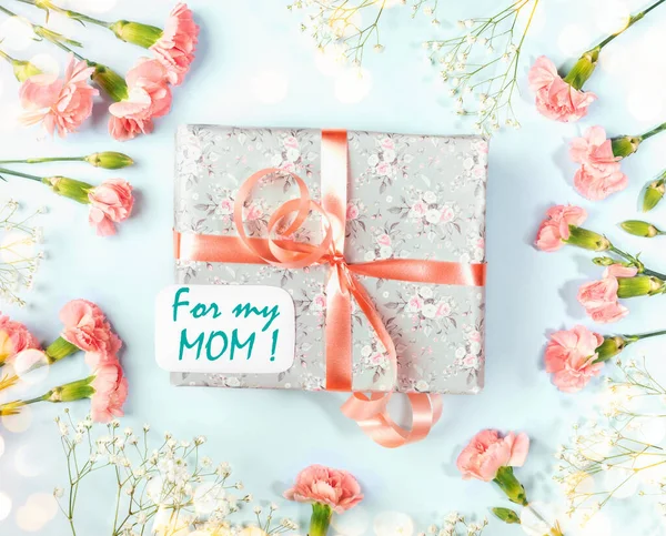 Gift box, For my mother note, frame of coral carnations and gypsophila on blue with bokeh lights. — Stock Photo, Image