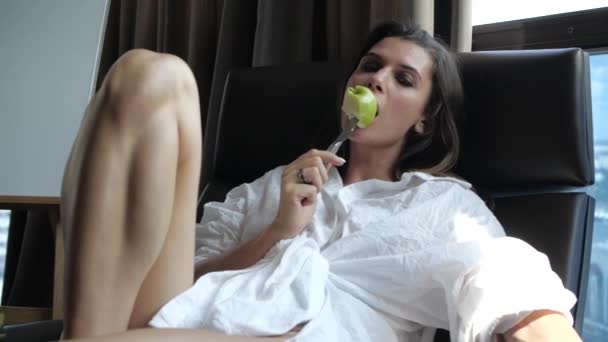 En moderne pige i en hvid skjorte spiser et æble lige fra en kniv – Stock-video