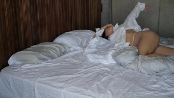 Femme en chemise et jambes nues repose sur un lit blanc dans une chambre d'hôtel — Video