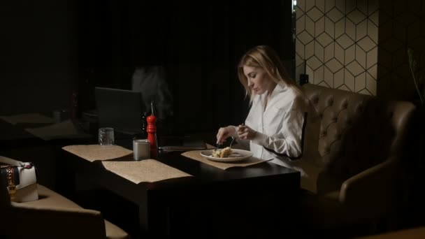 Een eenzame vrouw zit op een bank in een restaurant voedsel snijden en eten — Stockvideo
