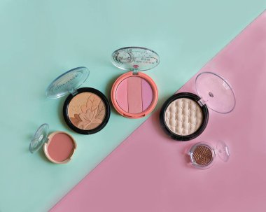 Hassas mavi ve pembe arka planda birden fazla allık ve pudra var. Pastel modayı renklendirme temeli