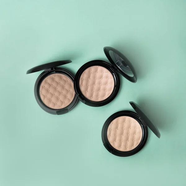 Multiple blush and compact face powders on a delicate blue background. Pastel trendy colors matte foundation