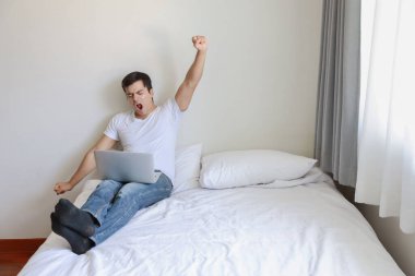 Beyaz gömlekli ve mavi kotlu akıllı beyaz bilgisayar kullanıyor ve yatak odasında yatağa uzanıyor (ev kavramında iş