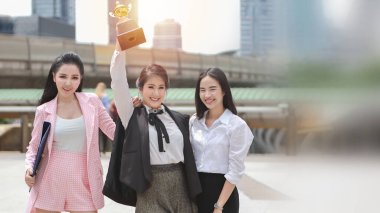 Zeki ve genç, güzel Asyalı iş kadını 3 grup ayakta ve ellerini kaldırarak kupa gösteriyorlar ve ofis inşa etme geçmişi, başarı başarısı ve kazanan kavramlarla kutlama yapıyorlar.