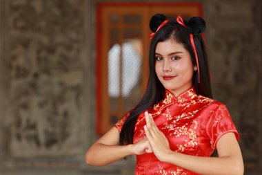 Kırmızı Çinli geleneksel Cheongsam Qipao elbisesi ve mutlu gülümseyen yüzüyle güzel bir Asyalı kadın, antik duvarın önünde duruyor (Çin yeni yılı konsepti))