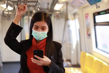 Yeni normal covid-19 salgını. Trendeki insanlardan virüs kapmasını önlemek için maske takan Asyalı genç bir kadın. Trende akıllı telefon iletişimi kullanıyor.