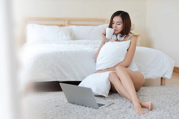 寝室でコーヒーや紅茶を飲みながらコンピュータ上で作業白いシャツの美しいアジアの女性の肖像画 — ストック写真