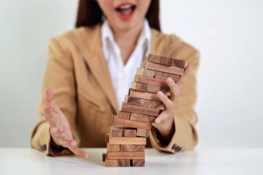 İş kadını, klasik süitte oturan ve düşen tahta blok dominolarını iş riski, yatırım sigortası veya iş risk kontrolü kavramından masaya yatırmayı durduran ellerini uzattı