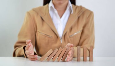 İş kadını, klasik süitte oturan ve düşen tahta blok dominolarını iş riski, yatırım sigortası veya iş risk kontrolü kavramından masaya yatırmayı durduran ellerini uzattı