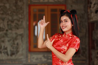 Kırmızı elbiseli güzel Asyalı kadın geleneksel Cheongsam Qipao ve gösteri jesti gri arka planda mutlu bir gülümseme ile bir şey (Çin yeni yıl konsepti)
