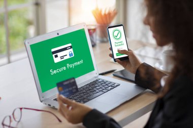 Bilgisayarlı ve akıllı cep telefonu kullanan Afrikalı bir kadın online ödeme veya ofis alışverişi için kredi kartı kullanıyor. İş kadını ödemeyi tamamladığı mesajını cihazda gösteriyor. Teknolojili yaşam biçimi