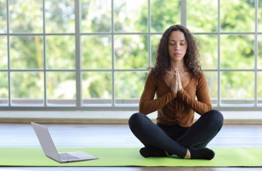Sportif Afro-Amerikalı kadın yerde oturup bilgisayardan antrenman videosu izleyerek yoga antrenmanı yapıyor. Sağlıklı bir kadın egzersiz yapıyor ve evde uzak bir ders alıyor.