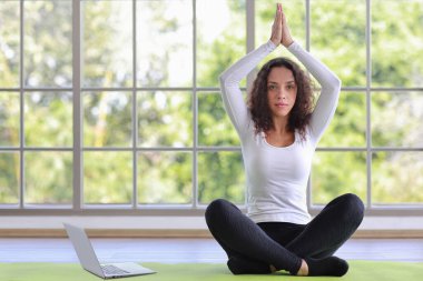 Sportif Afro-Amerikalı kadın yerde oturup bilgisayardan antrenman videosu izleyerek yoga antrenmanı yapıyor. Sağlıklı bir kadın egzersiz yapıyor ve evde uzak bir ders alıyor.