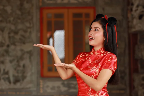 赤いドレスを着た美しいアジアの女性伝統的なChongsam Qipaoと灰色の背景に幸せな笑顔の顔を持つ何かを示すジェスチャー 中国の新年のコンセプト — ストック写真