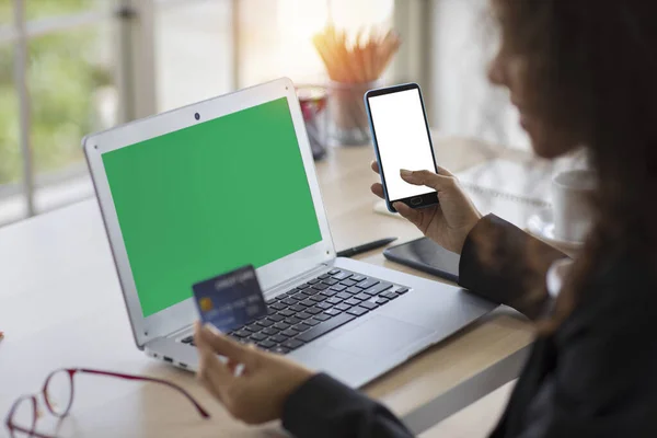 African woman using computer and smart mobile phone with credit card for online payment or shopping at the office. Businesswoman show green and white empty screen on device. Lifestyle with technology