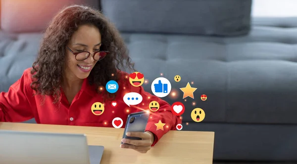 Happy smiling latin woman in living room using internet on smart mobile phone with social media interaction, notification icons, wow, like, love, and message above device. Lifestyle with technology