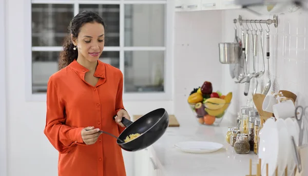 Happy latin woman cooking, smelling and tasting food while making meal in kitchen. Beautiful young female with headphone prepare delicious meal and listen music at home. Healthy and lifestyle concept
