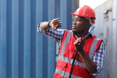 Foreman, kol saati kontrol kutusuna bak ve konuş. Profesyonel mühendis ya da güvenlik şapkalı işçi konteyner kargo alanında çalışıyor ve endüstriyel konteynır kargo gemisini kontrol ediyor..