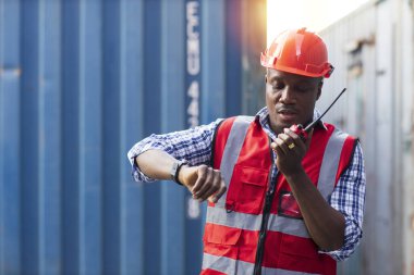 Foreman, kol saati kontrol kutusuna bak ve konuş. Profesyonel mühendis ya da güvenlik şapkalı işçi konteyner kargo alanında çalışıyor ve endüstriyel konteynır kargo gemisini kontrol ediyor..
