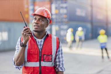 Ustabaşı mühendisi telsiz uzaktan kumandalı konteynır yükleme kutusu kullanıyor. Konteyner kargo alanındaki kask işi ve endüstriyel konteynır kargo gemisini kontrol eden kendinden emin mühendislik.