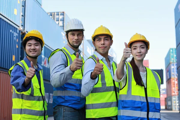 Group of multiethnic technician engineer or worker in protective uniform with hardhat standing and showing thumb up celebrate successful together or completed deal commitment at container cargo site