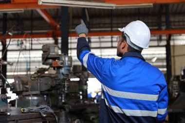 Arka görüş teknisyeni koruyucu giysi mühendisi ayakta ve telsiz kullanarak ağır sanayi imalat fabrikasında metal torna işletim makinesini kontrol ediyor veya onarıyor.