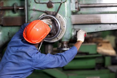 Ağır endüstri imalat fabrikasında endüstriyel makine işlemini kontrol ederken ayakta duran ve bilgisayar kullanan koruyucu teknisyen mühendisi.