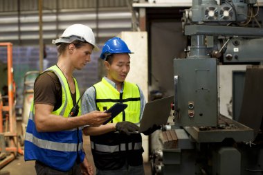 Ağır endüstri imalat fabrikasında bilgisayarlı makine denetimini kullanmak üzere çıraklara ya da iş arkadaşlarına eğitim veren koruyucu üniformalı teknisyen.