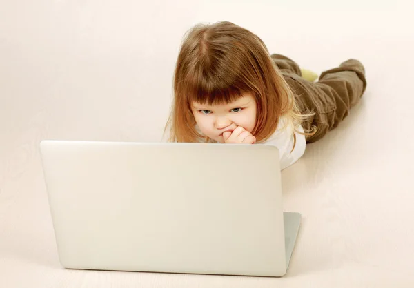 Una bambina con un portatile sdraiata sul pavimento — Foto Stock