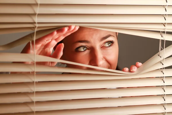 Ritratto di una donna che guarda attraverso le tende — Foto Stock