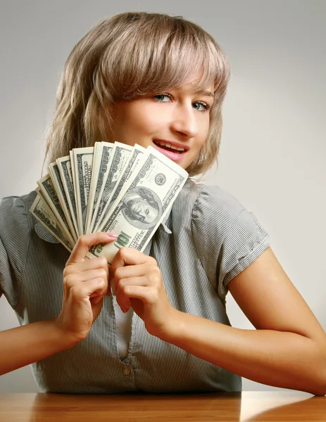 Mladá žena sedí na stole a držet dolary, — Stock fotografie
