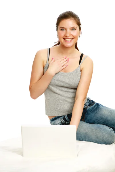 Ragazza eccitata in jeans con computer portatile seduto sul suo letto isolato — Foto Stock