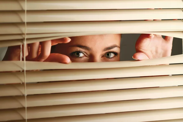 Femme regardant à travers les stores — Photo