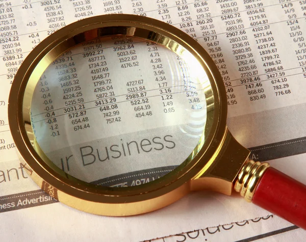Looking through magnifying glass to financial report — Stock Photo, Image
