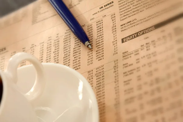 Closeup of a cup of coffee and a pen on a morning newspaper — Stock Photo, Image