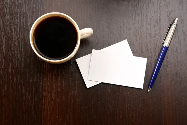 Una taza de café, tarjetas vacías y un bolígrafo sobre una mesa de madera —  Fotos de Stock