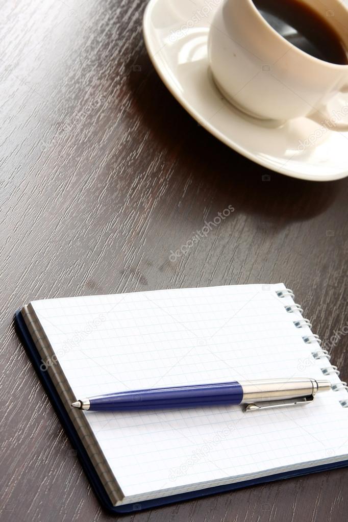 Cup of coffee and a notebook with a pen on a wooden table