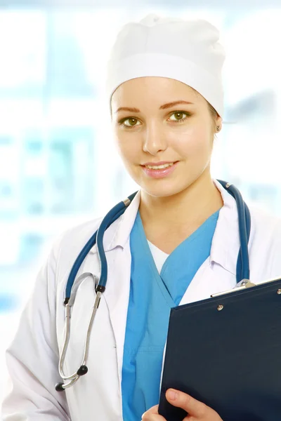 A smiling female doctor with a folder in uniform indoors — Stock Photo, Image