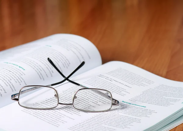 Buch mit Brille auf dem Schreibtisch gegen Bücher — Stockfoto