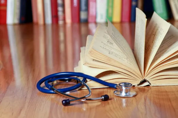 Un estetoscopio está acostado con un libro sobre el escritorio contra libros . —  Fotos de Stock