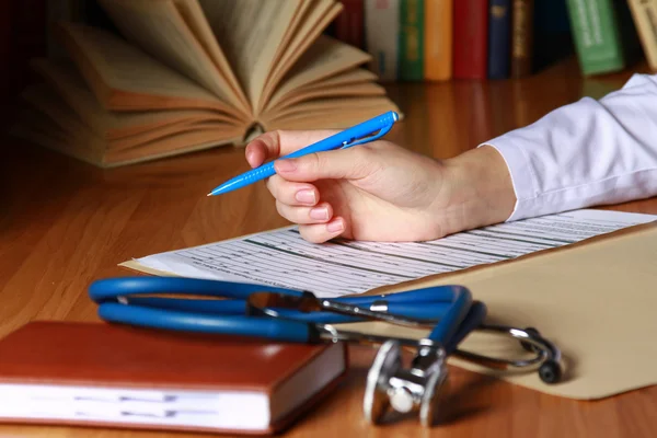 Close-up of writing doctor's hands on a wooden desk. — Stock Photo, Image