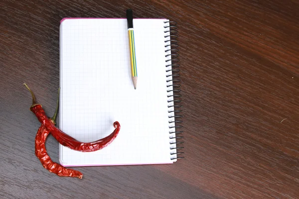Peppers near a notebook and a pencil, — Stock Photo, Image